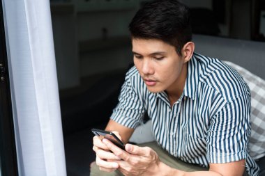 Asyalı bir adam kanepede oturmuş akıllı telefonuyla oyun oynuyor..