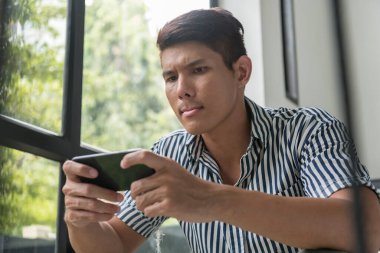 Asyalı bir adamın portresi merdivenlerde oturmuş akıllı telefondan ciddi görünümlü cep telefonu oyunu oynuyor..