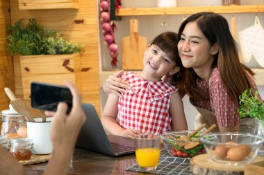 Asyalı anne ve kızı mutfakta akıllı telefonla fotoğraf çekiyor..