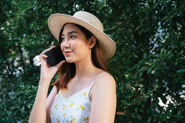 美しいアジアの旅行者の女性は 公園で電話で話す帽子と白いドレスを着用 — ストック写真