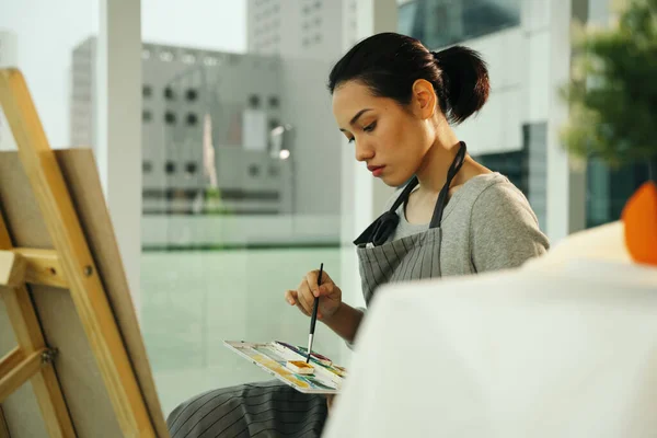 Female artist painting colour oil on canvas easel in studio.