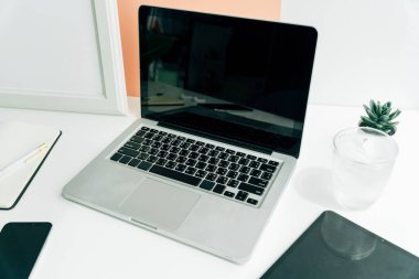 Boş ekran dizüstü bilgisayarı ve buz gibi suyu olan minimum beyaz oda çalışma alanı.