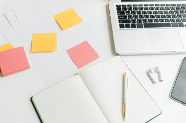 Üst görünüm - Boş kitap, akıllı telefon, dizüstü bilgisayar, kulaklık, notlar içeren en az çalışma masası.