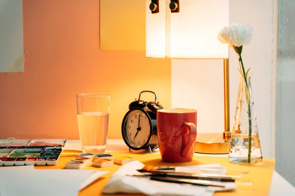 Artist working desk with many painting equipment in warm light.