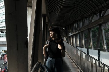 Sırt çantalı Asyalı kadın üstgeçitte yürüyor Bangkok 'taki yola bakıyor.