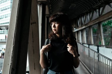 Sırt çantalı Asyalı kadın üstgeçitte yürüyor Bangkok 'taki yola bakıyor.