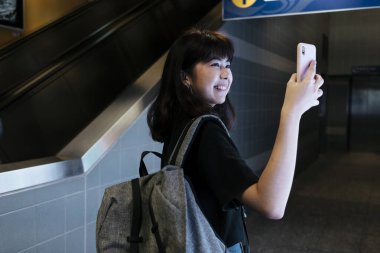 Neşeli Asyalı Taylandlı sırt çantalı kadın metro istasyonunda cep telefonu kullanıyor..