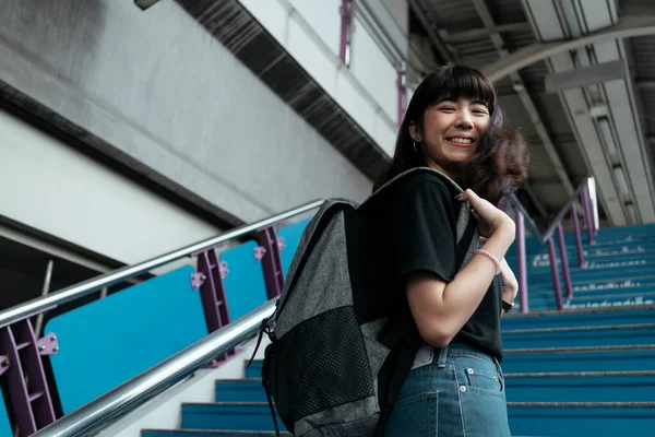 Asian woman teenager walking on blue stair at train station platform in Bangkok city. Thai female backpacker travel alone.