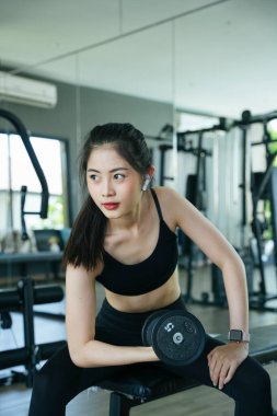 Sağlıklı Asyalı kadın halterle egzersiz yapıyor ve spor salonunda müzik dinliyor..