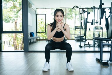 Sağlıklı Asyalı kadın egzersizi spor salonunda çömeliyor.