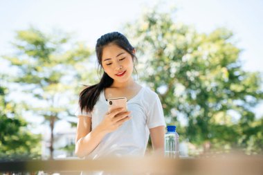 Sağlıklı Asyalı kadın koştuktan sonra akıllı telefon kullanıyor..