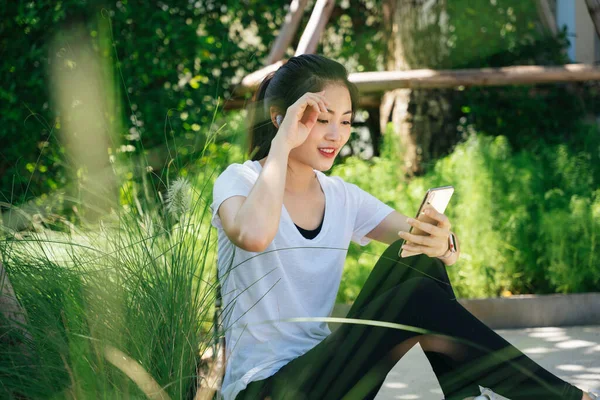 Healthy asian woman take a break using smartphone in park.