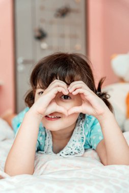 Küçük kız yatak odasındaki parmaklarıyla kalp işareti yapıyor..