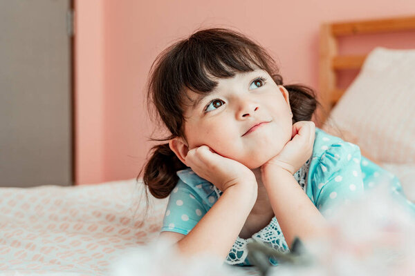 Close up portrait - little girl on bed looking at the window in bedroom.