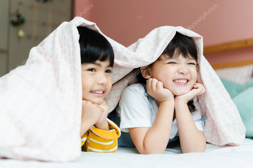 Boy and girl having fun stay under blanket in bedroom.