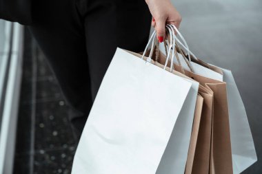 Şehirde alışveriş yaparken alışveriş torbaları tutan bir kadın. Alışveriş merkezinde elinde kahverengi beyaz alışveriş torbaları olan bir kadın..
