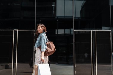 Caddedeki binanın girişinde elinde kese kâğıdıyla yürüyen neşeli Asyalı Taylandlı kadın..