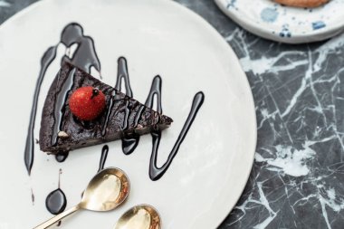 Çikolata soslu ve çilekli, beyaz tabakta, mermer masada nefis çikolatalı kek. Pastanın yanında iki altın kaşık.