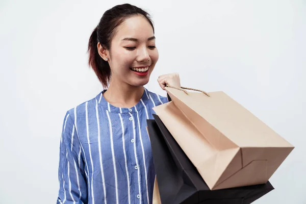 穿着蓝色衬衫的快乐的亚洲女人 手里拿着白色背景的购物袋 — 图库照片