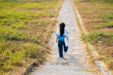 Beyaz ve mavi kravatlı siyah saçlı kızın arka planı otlaktaki taş merdivenlerden aşağı doğru yürür..