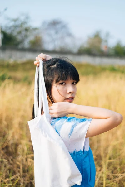 黒半分縛ら毛の女の子で白と青のネクタイ染料スタンディングで草原とホールドキャンバスバッグで彼女の背中 — ストック写真