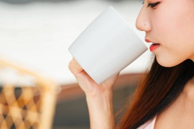 Yan görünüm portresi yakın - fincandan kahve içen genç Asyalı kadın. Modifiye et ve uzayı kopyala.