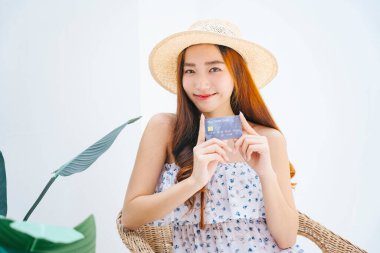 Asyalı güzel bir kadının portresi. Şapkalı ve beyaz elbiseli, elinde kredi kartı var..