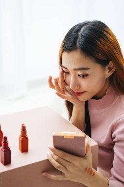 Güzel Asyalı kadın makyaj yapıyor ve taşınabilir aynaya bakıyor..