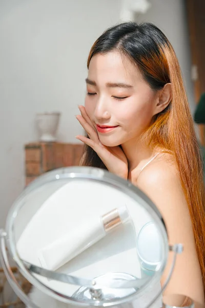 若いですアジアの女性適用クリームローションオン彼女の顔で自然光 — ストック写真