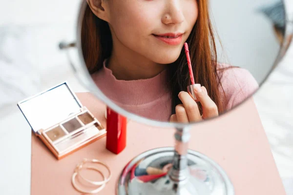 Beautiful asian woman applying lipstick infront of the mirror at home.