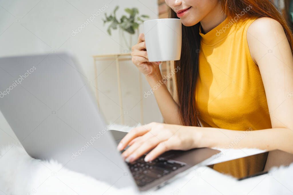 Young asian woman working on laptop computer and holding a cup of coffee.