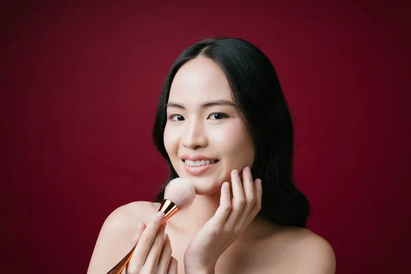 美しいです若いですアジアの女の子ともに化粧ブラシのために自然メイク孤立した赤の背景 — ストック写真