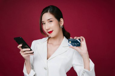 Beyaz ceketli güzel bir Asyalı kadının portresi. İnternetten akıllı telefon ve kredi kartıyla alışveriş yapıyor..