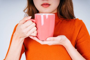 Elinde kahve fincanı ya da fincanı olan turuncu kazaklı Asyalı kadın..