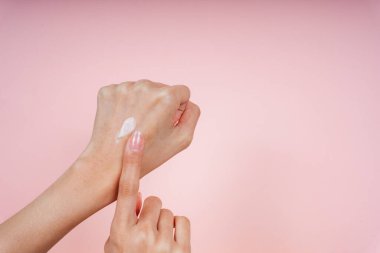 Güzel bir kadın krem sürerken arka eliyle pembe arka planda izole ediyor..