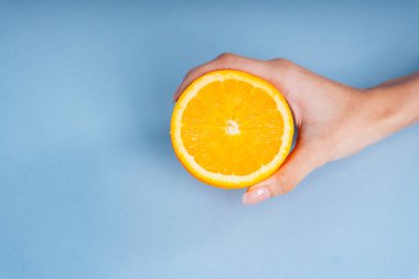 Mavi arka planda bir dilim portakal tutan bir kadın..