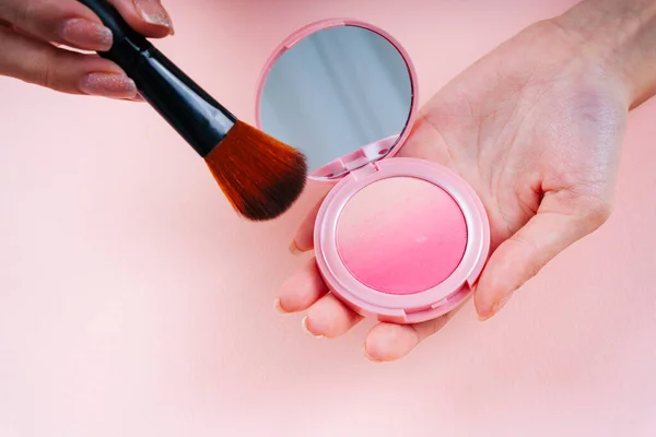 Close up of makeup brush and blush box isolated on pink background.