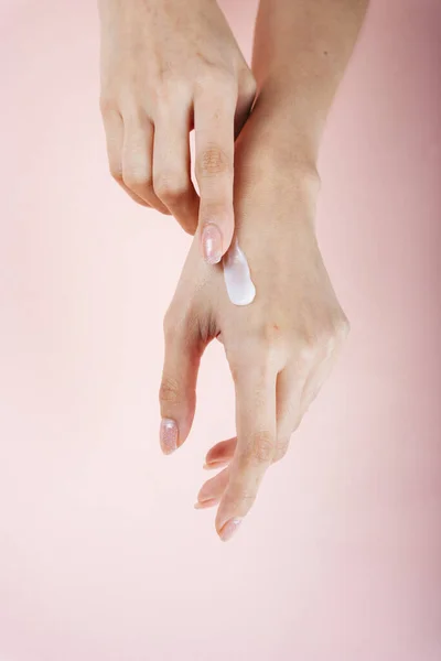 Woman hand applying lotion cream isolate on pink background.