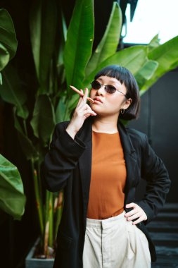 Havalı Asyalı kısa saçlı kadın sigara gibi kalem tutan güneş gözlüğü takıyor..