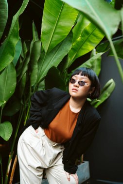 Bahçede güneş gözlüğü takan kısa saçlı genç Asyalı kadının portresi..