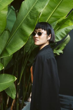 Bahçede güneş gözlüğü takan kısa saçlı genç Asyalı kadının portresi..