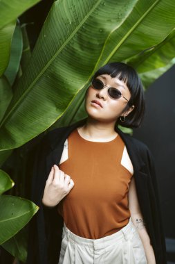 Bahçede güneş gözlüğü takan kısa saçlı genç Asyalı kadının portresi..
