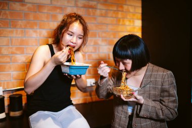 Mutfakta baharatlı erişte yiyen iki Asyalı kadın..