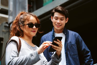 Akıllı telefondan dijital haritaya bakan Asyalı çift. İkisi de şehirde geziyor..