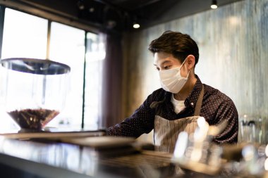 Maske takan Asyalı barmen, Covid-19 salgınında barın arkasında kahve yapıyor. İşletme yeniden açılıyor.