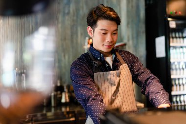 Kafenin arkasında makineyle kahve yapan Asyalı barmen..