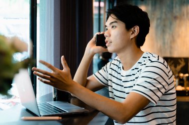 Kafede dizüstü bilgisayar ve akıllı telefonla çalışan Asyalı bir serbest yazar..