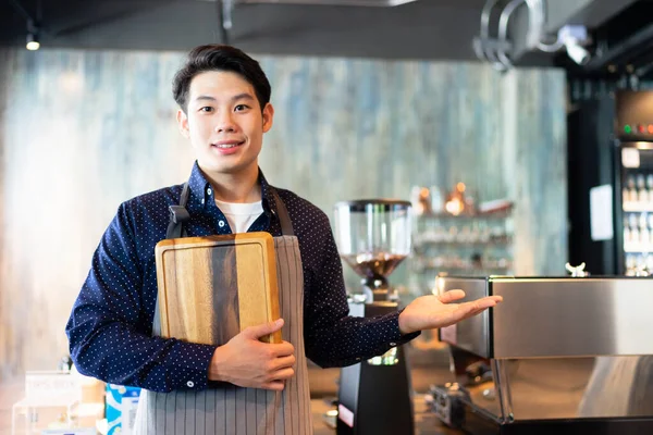 Portrait of young asian waiter holding wooden tray show hand empty hand for product.
