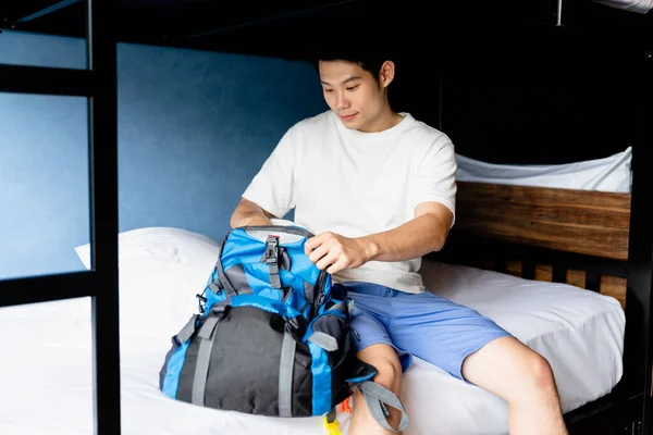 Backpacker asian man putting clothes in the bag at hotel before check out.
