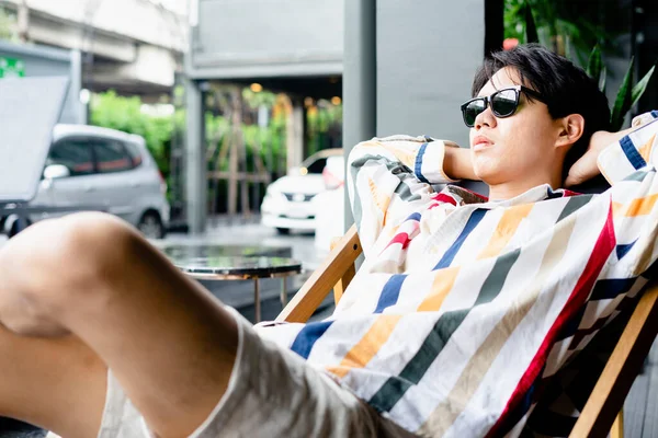 戴太阳镜的亚洲年轻人在酒店的海滩椅子上放松一下 — 图库照片